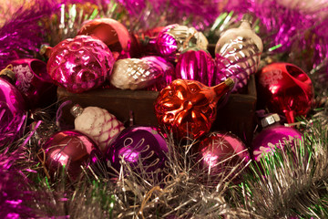 New Year's round glass toys, vintage red and pink Christmas tree decorations lie in a wooden box surrounded by a shiny garland. Christmas background, concept