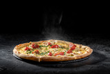 Fototapeta Tulipany - Hot tasty traditional italian pizza with salami, cheese, tomatoes greens on a dark background
