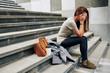 Pretty young woman sitting on steps outdoor and covering face when crying after difficult break up