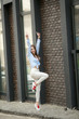 © ElenaBatkova - Stylish young woman in white jeans walks and bounces on city streets against brick wall.