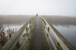 A woman walking on a small footbridge on a foggy day in autumn.