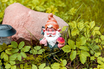 Figure of a garden gnome in the grass on a blurred background of decorative stone. Selective focus.