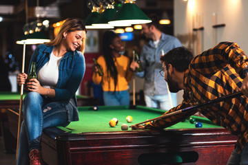 Wall Mural - Four smiling friends in bar playing billiard together.