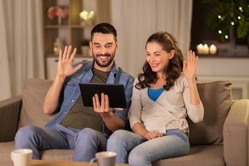 Poster - technology, communication and people concept - smiling happy couple with tablet pc computer having video call at home in evening