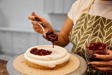 Wall Mural - Cropped view of confectioner adding tasty berry jam on cake