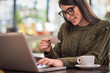 © chika_milan - Attractive caucasian brunette in sweater sitting in cafe, typing on keyboard and holding credit card.