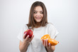 © studioprodakshn - young attractive woman holding two halves of oranges in one hand and red apple in another looking surprised on isolated white background dietology and nutrition