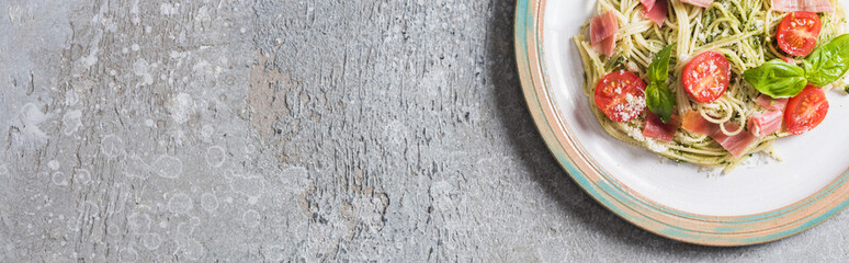 Wall Mural - top view of cooked Pappardelle with tomatoes, basil and prosciutto on plate on grey surface, panoramic shot