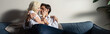 © LIGHTFIELD STUDIOS - Panoramic shot of smiling young couple hugging on sofa in living room