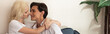 © LIGHTFIELD STUDIOS - Side view of smiling couple embracing on sofa in living room, panoramic shot