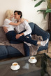 © LIGHTFIELD STUDIOS - Selective focus of smiling couple hugging on sofa beside coffee cups on table