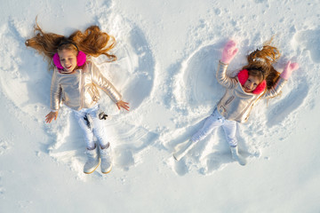  Snow angels made by a kids in the snow. Smiling children lying on snow with copy space. Funny kids making snow angel. Top view.