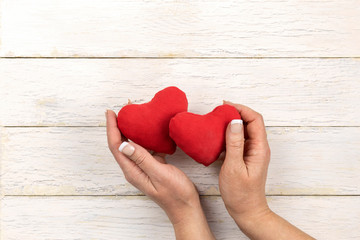 Female hands holding two red hearts on old white wooden table. Concept of celebrating Valentine's day. Top view, flat lay.