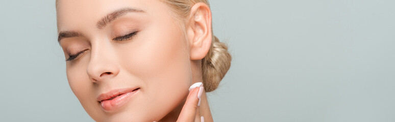 Wall Mural - panoramic shot of happy woman applying face cream isolated on grey