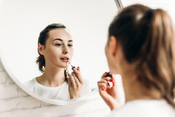 Woman putting on lipstick in bathroom.