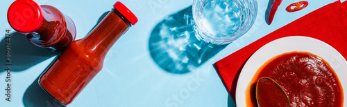 Cuadros en Lienzo Top view of ketchup in plate and bottles beside chili pepper and glass of water