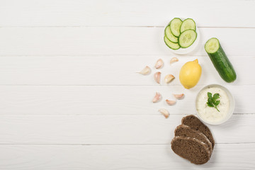 Canvas Print - Top view of tzatziki sauce with organic ingredients and bread on white wooden background