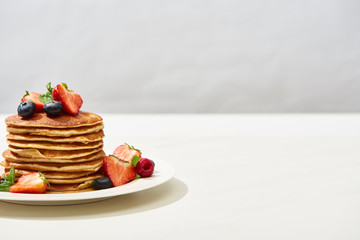 Wall Mural - delicious pancakes with blueberries and strawberries on plate on white surface isolated on grey