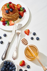 Wall Mural - top view of delicious pancakes with honey, blueberries and strawberries on plate near fork and knife on marble white surface