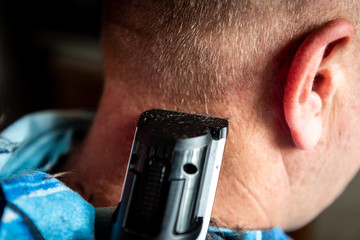 Hairdresser cuts man's hair with electric clipper trimmer.