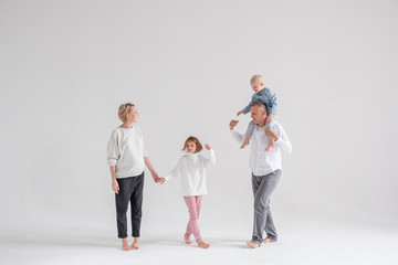 Cheerful funny young family mom dad daughter and son posing in the studio barefoot on a white background. Concept of warm family relationships. Copyspace