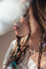 Wall Mural - tender girl with closed eyes and braids in hairstyle posing in white boho dress on grey with lens fl