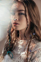Wall Mural - attractive ethnic girl with braids in hairstyle posing in white boho dress on grey with lens flares