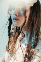 Wall Mural - tender girl with braids in hairstyle posing in white boho dress on grey with lens flares
