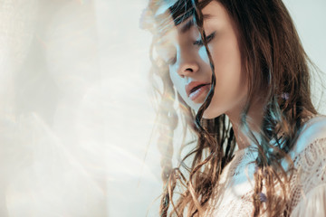 Wall Mural - tender young woman with braids in hairstyle posing in white boho dress on grey with lens flares