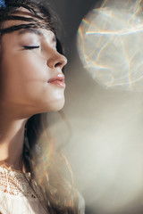 Wall Mural - attractive boho girl with braids in hairstyle posing with closed eyes on grey with lens flares