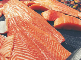 Sliced raw salmon or fresh salmon. Salmon fillets for sale at market displayed with a patchwork effect. Many fresh salmon fish meat slices in a black tray which are sale in the supermarket.