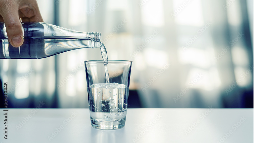 Nalewanie oczyszczonej świeżej wody do picia z butelki na stole w salonie - obrazy, fototapety, plakaty 