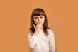 © Marharyta Hanhalo - Mistake or wrong answer, little girl child is worried and stressed because she said something wrong. Covers his mouth with his hand over orange background