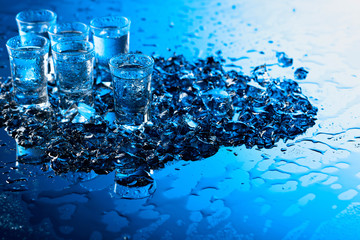 Damp glasses of vodka with ice on a black reflective background.