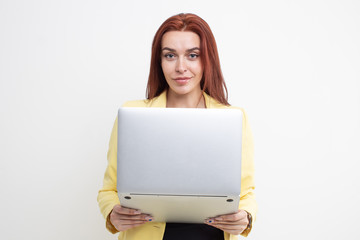 Wall Mural - Red-haired girl in a yellow suit holding a laptop on a white background