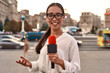 © Svitlana - 24 Hour News Source. TV reporter presenting the news outdoors. Journalism industry, live streaming concept.