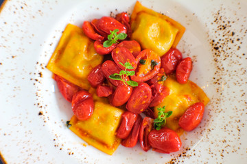 top view of plate of handmade Caprese ravioli served with red corbarino cherry tomato and marjoram