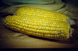 Patch of corn peeled on a wooden board on a background of leaves. Vignette