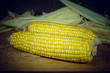 Patch of corn peeled on a wooden board on a background of leaves. Vignette