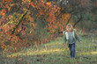 © ElenaBatkova - A cheerful child walks in the autumn in a garden with trees covered with a yellow leaf.