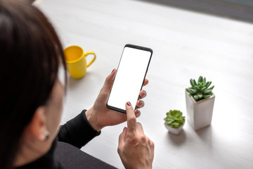 Poster - Woman holding smart phone with isolated screen for mockup, app or web site presentation. Desk with cup of coffee and plants i background