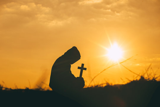 Man sit down and praying with holding the cross in hand at sunset background. christian silhouette concept.