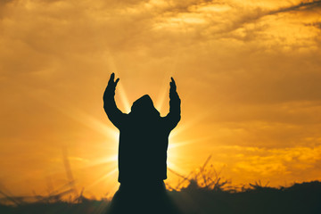 Wall Mural - Man raise two hands to sky for praying to God at sunset background. christian silhouette concept.