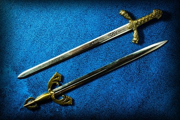 Two knightly swords lie in parallel on a dark blue background. View from above