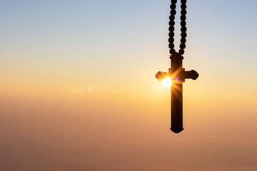 Silhouettes of crucifix necklace symbol with bright sunbeam on the colorful sky background