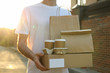 Man holds blank box, coffee cups and paper package outdoor. Delivery