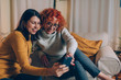 © cherryandbees - woman friends sitting sofa at home talking, using mobile phone,
