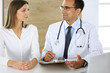 © Iryna - Doctor and patient discussing the results of a physical examination while sitting at a desk in a clinic. A male doctor using a clipboard to fill out a medical history of a young woman's medication