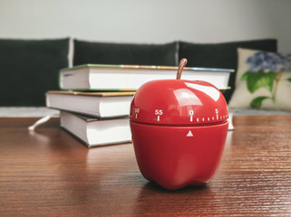 Studying with pomodoro technique with a kitchen timer in a shape of an apple for timing the study sessions and increasing productivity with books in the background