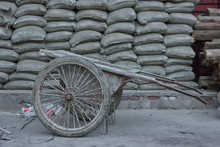 Old Construction Barrow Standing In Front Of Cement And Sand Bags Pile.